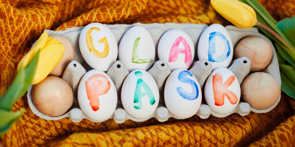 Ägg i kartong som har färgglada bokstäver som bildar ordet Glad Påsk